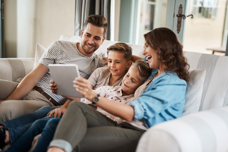 Family of 4 playing on large tablet together on couch.
