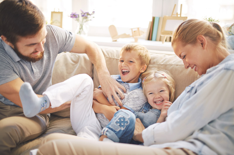 Family of 4 playing happily on couch.